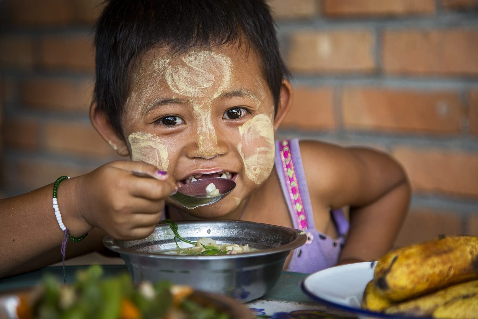 Young asian girl sits eating soup from a metal bowl.