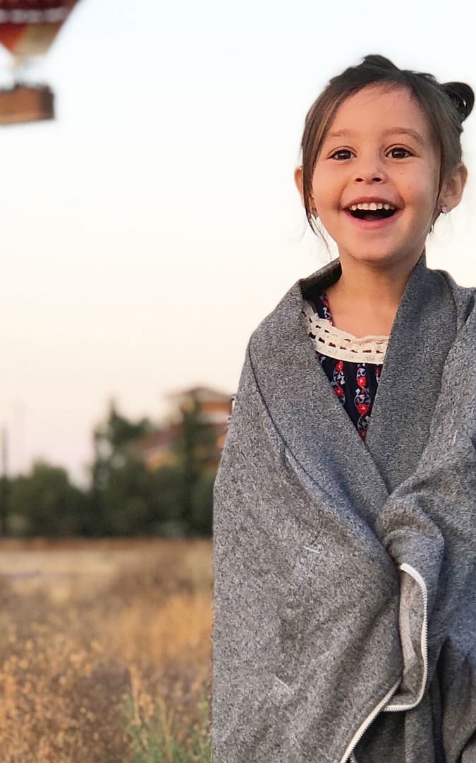 Happy girl smiling with a grey blanket wrapped around her with hot air balloons in the background